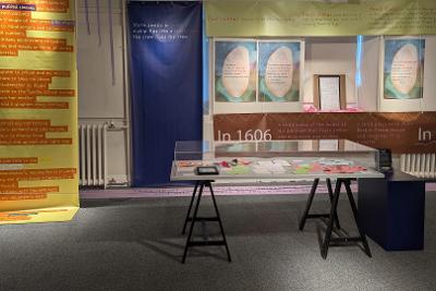 Photograph of FOUND exhibition showing PVC banners and a glass case full of paper notes